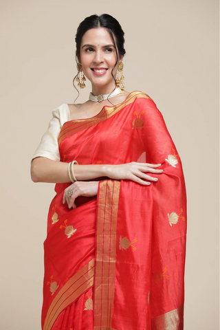 Woman wearing a red saree with gold patterns on a beige background