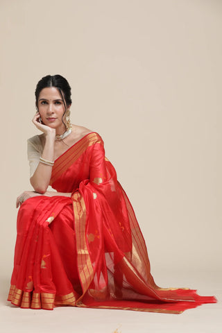 Woman wearing a red saree with gold border on a beige background