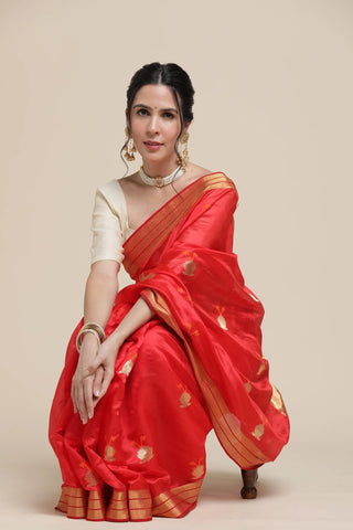 Woman wearing a red saree with gold patterns on a beige background
