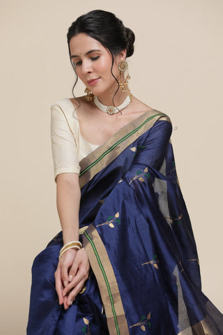 Woman wearing a blue saree with green and gold border on a beige background