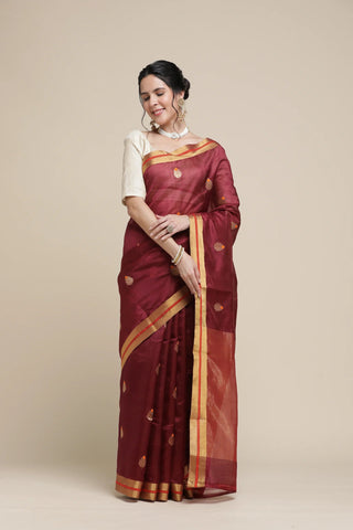 Woman wearing a maroon saree with gold border on a beige background