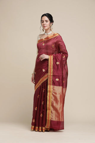 Woman wearing a maroon saree with gold border on a beige background