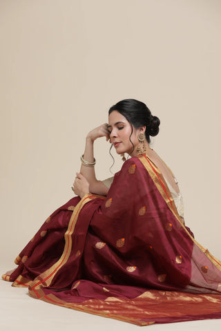 Woman wearing a maroon saree with gold patterns on a beige background