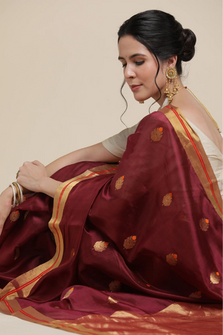 Woman wearing a maroon saree with gold patterns on a beige background