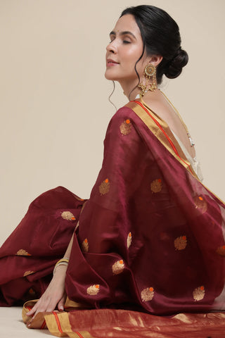 Woman wearing a maroon saree with gold patterns on a beige background