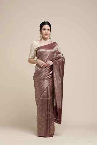 Woman wearing a brown saree with a white blouse against a beige background