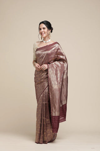 Woman wearing a brown saree with a white blouse against a beige background
