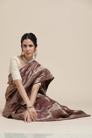 Woman wearing a brown saree with a white blouse on a beige background