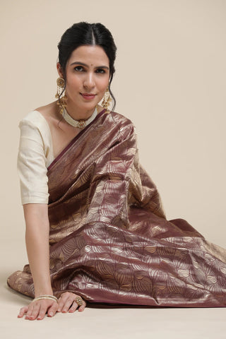 Woman wearing a brown saree with a white blouse against a beige background