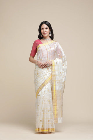 Woman wearing a white saree with yellow border and pink blouse against a beige background