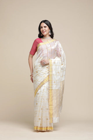 Woman wearing a white saree with gold border and pink blouse against a beige background