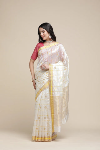Woman wearing a white saree with yellow border on a beige background