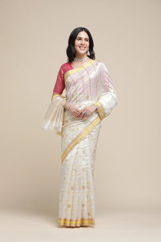 Woman wearing a white saree with gold border and red blouse against a beige background