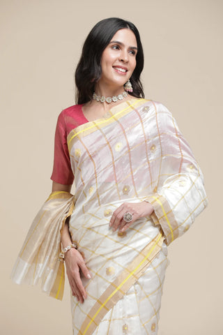 Woman wearing a white saree with gold border and red blouse against a beige background