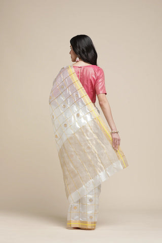 Woman wearing a white saree with gold patterns and a pink blouse against a beige background