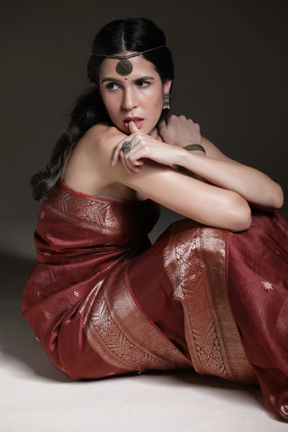 Woman in a traditional red saree with intricate patterns, sitting on a dark background.