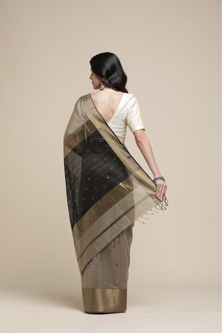 Woman wearing a black and beige saree with a plain background