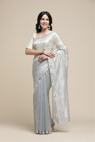 Woman wearing a light gray saree with a white blouse against a beige background