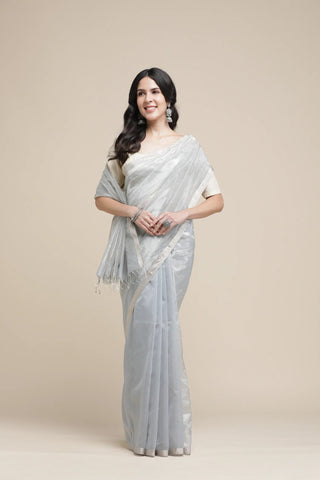 Woman wearing a light gray saree with a plain background