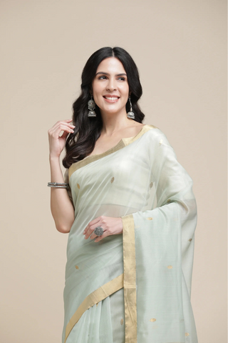 Woman wearing a light green saree with a beige border on a beige background