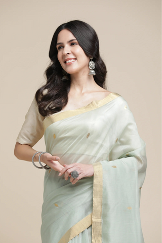 Woman wearing a light green saree with a beige border on a beige background