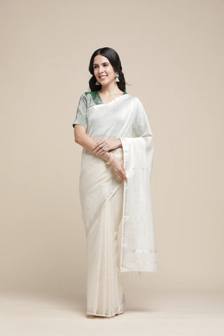 Woman wearing a white saree with a green blouse against a beige background
