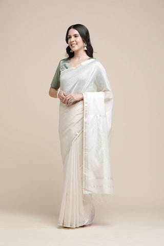 Woman wearing a white saree with a green blouse against a beige background