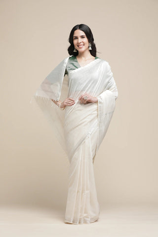 Woman wearing a white saree with a green blouse against a beige background