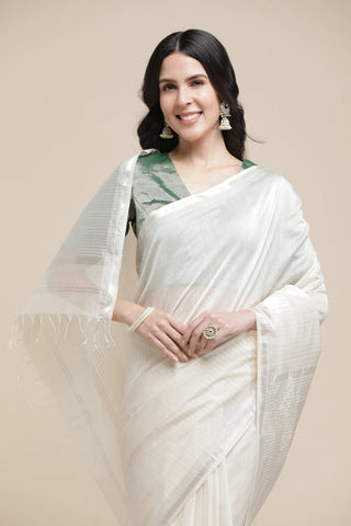 Woman wearing a white saree with green blouse against a beige background