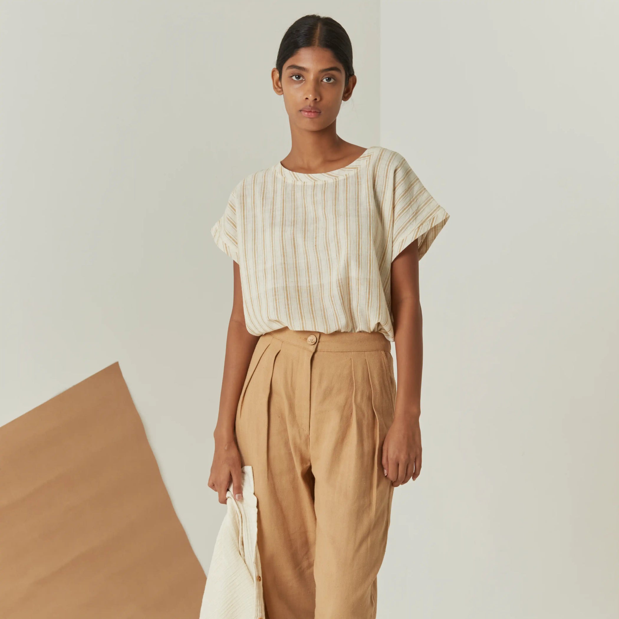 Woman wearing a striped shirt and beige pants against a plain background